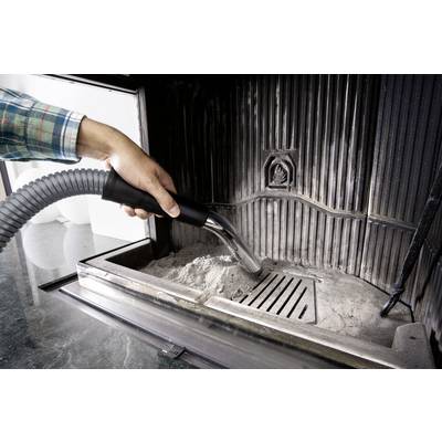Eine Person reinigt die Asche aus einem Kamin mit einem Staubsauger. Der Kamin ist aus Metall, und das Bild zeigt den Reinigungsprozess.