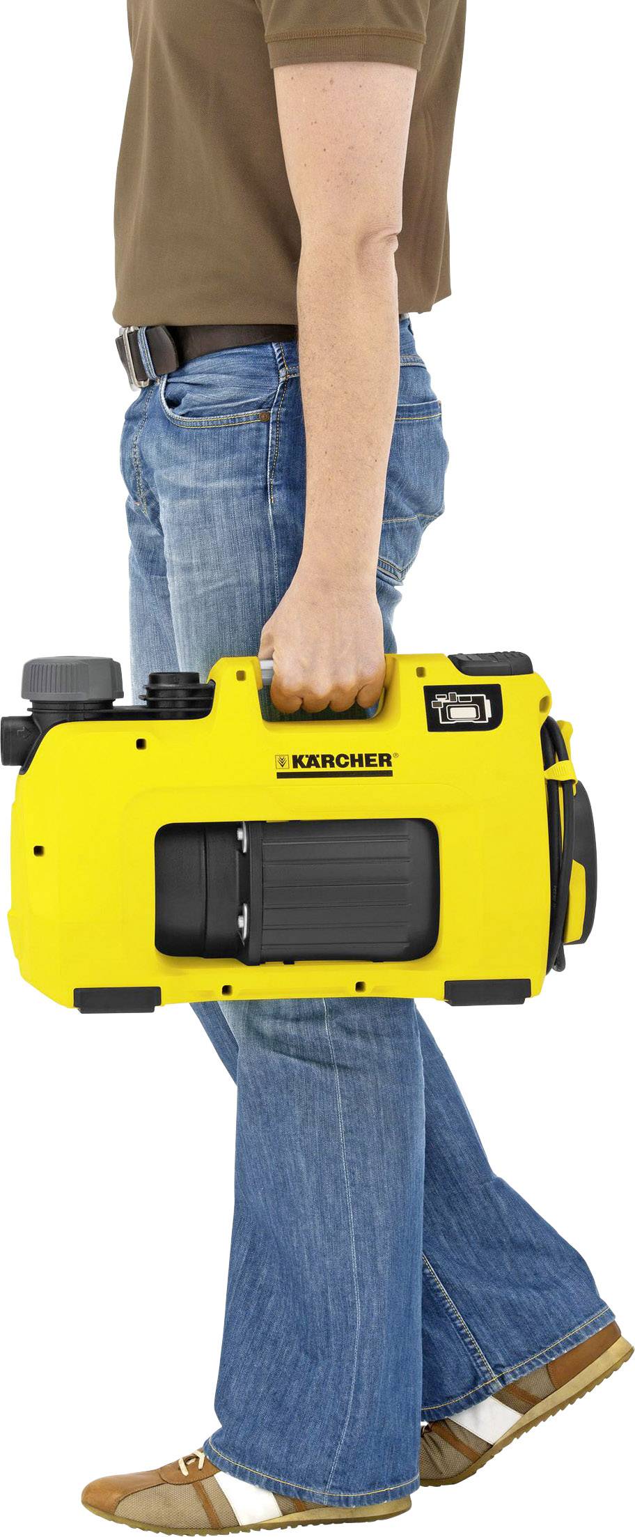 Eine Person trägt einen gelben tragbaren Hochdruckreiniger in der Hand, sichtbar sind Jeans und braune Schuhe.