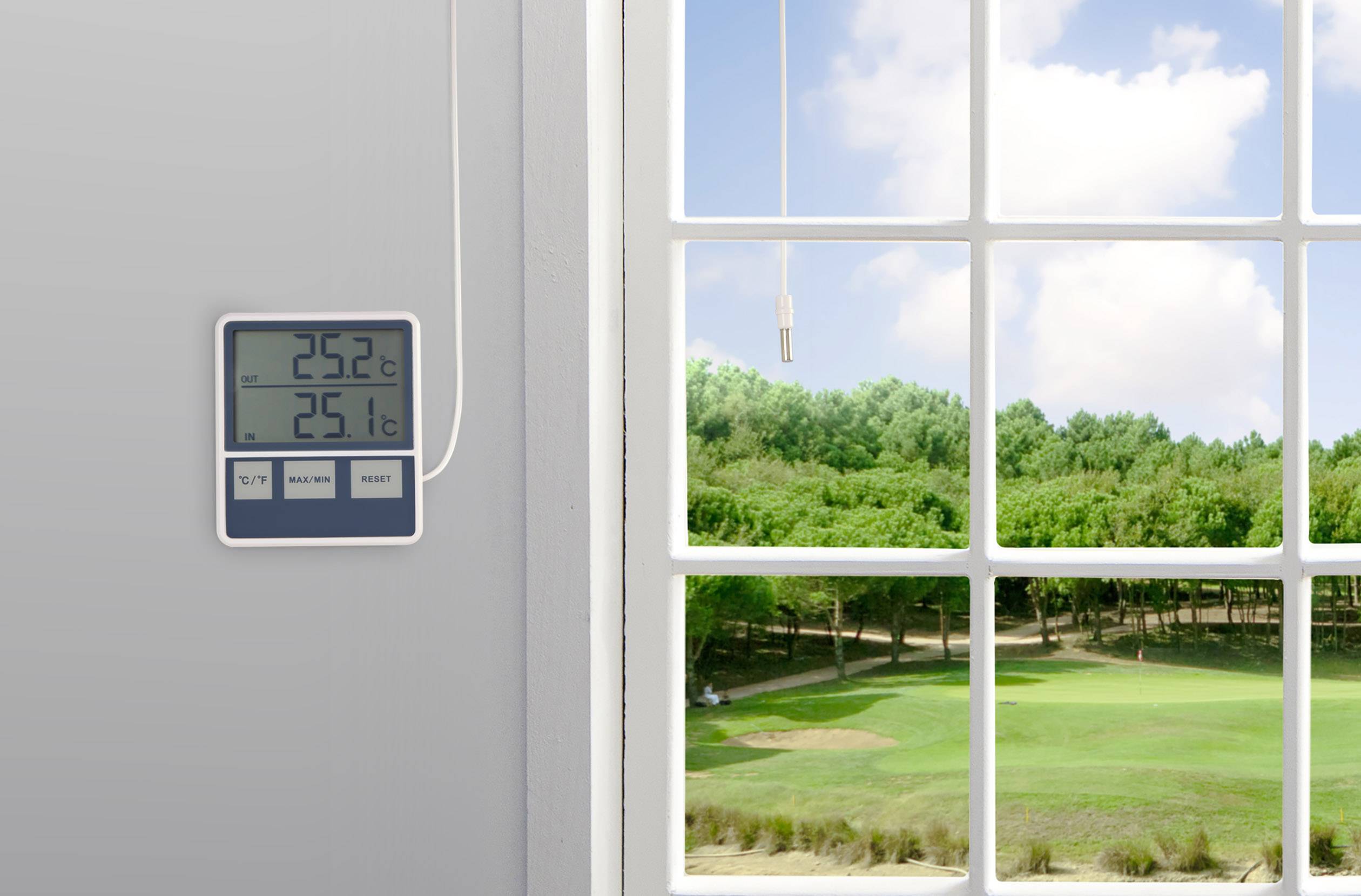 Ein Thermometer an der Wand zeigt 25,2°C Raumtemperatur und 25,1°C Außentemperatur an. Draußen ist ein Golfplatz unter blauem Himmel zu sehen.