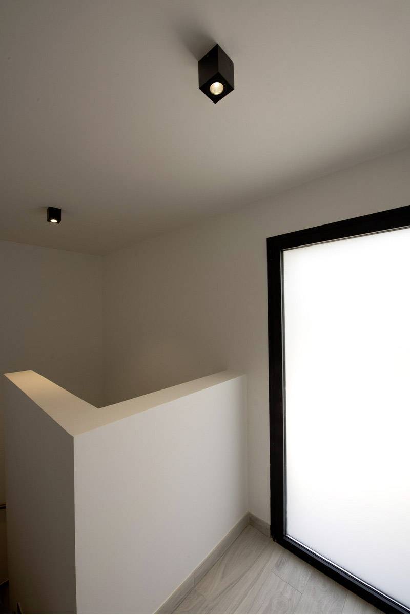 Minimalistischer Raum mit weißen Wänden und Boden in Holzoptik. Deckenleuchten sind an der schlichten Decke montiert.