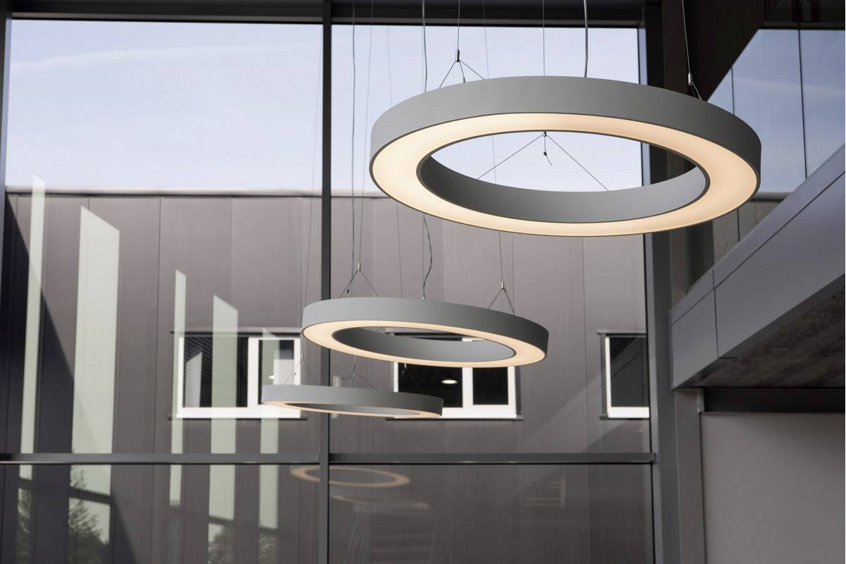 Große, runde Pendelleuchten hängen von der Decke in einem modernen Gebäude mit Glasfenstern und grauen Wänden.