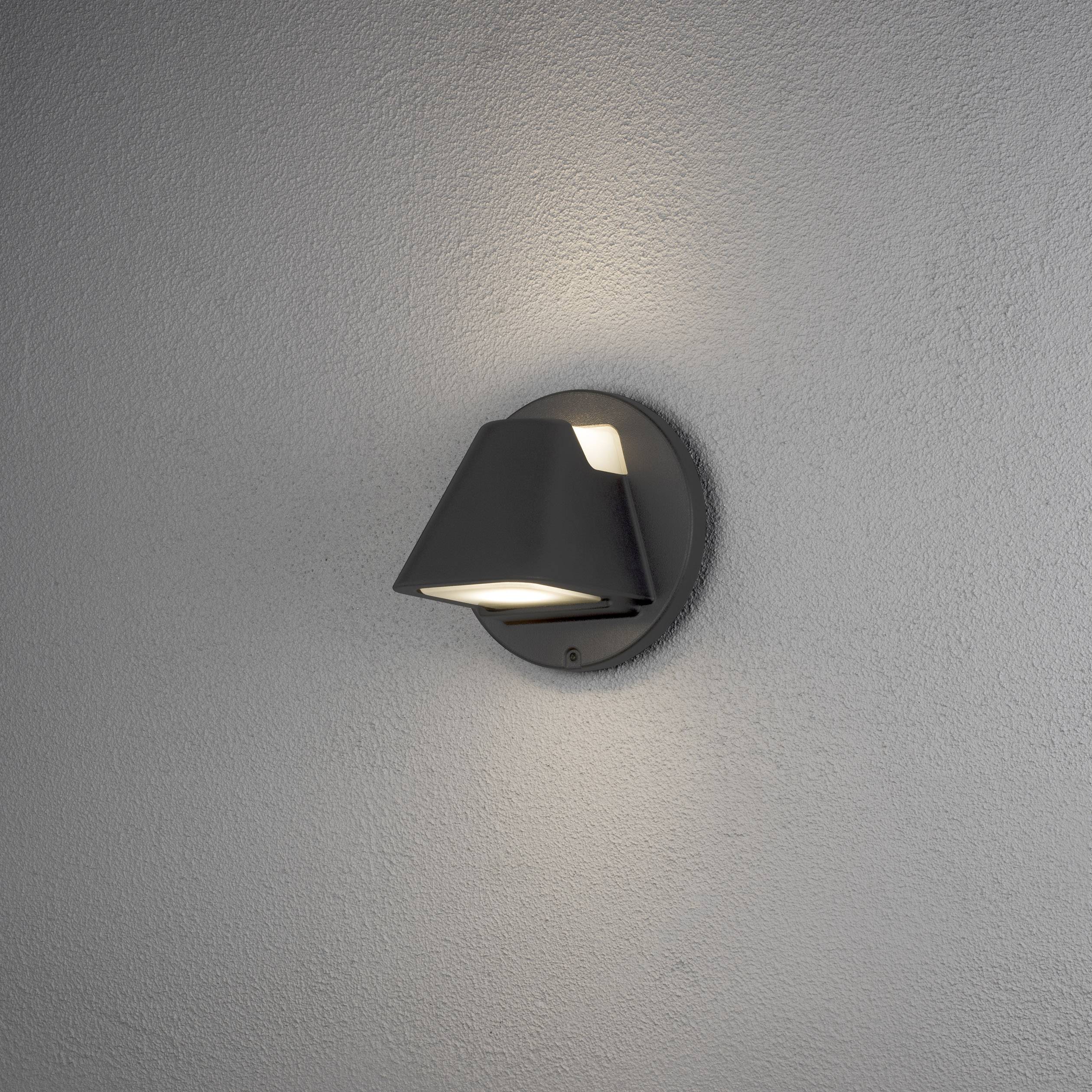 Eine Wandlampe mit kegelförmigem Schirm wirft warmes Licht auf die graue Wand und erzeugt eine atmosphärische Beleuchtung.