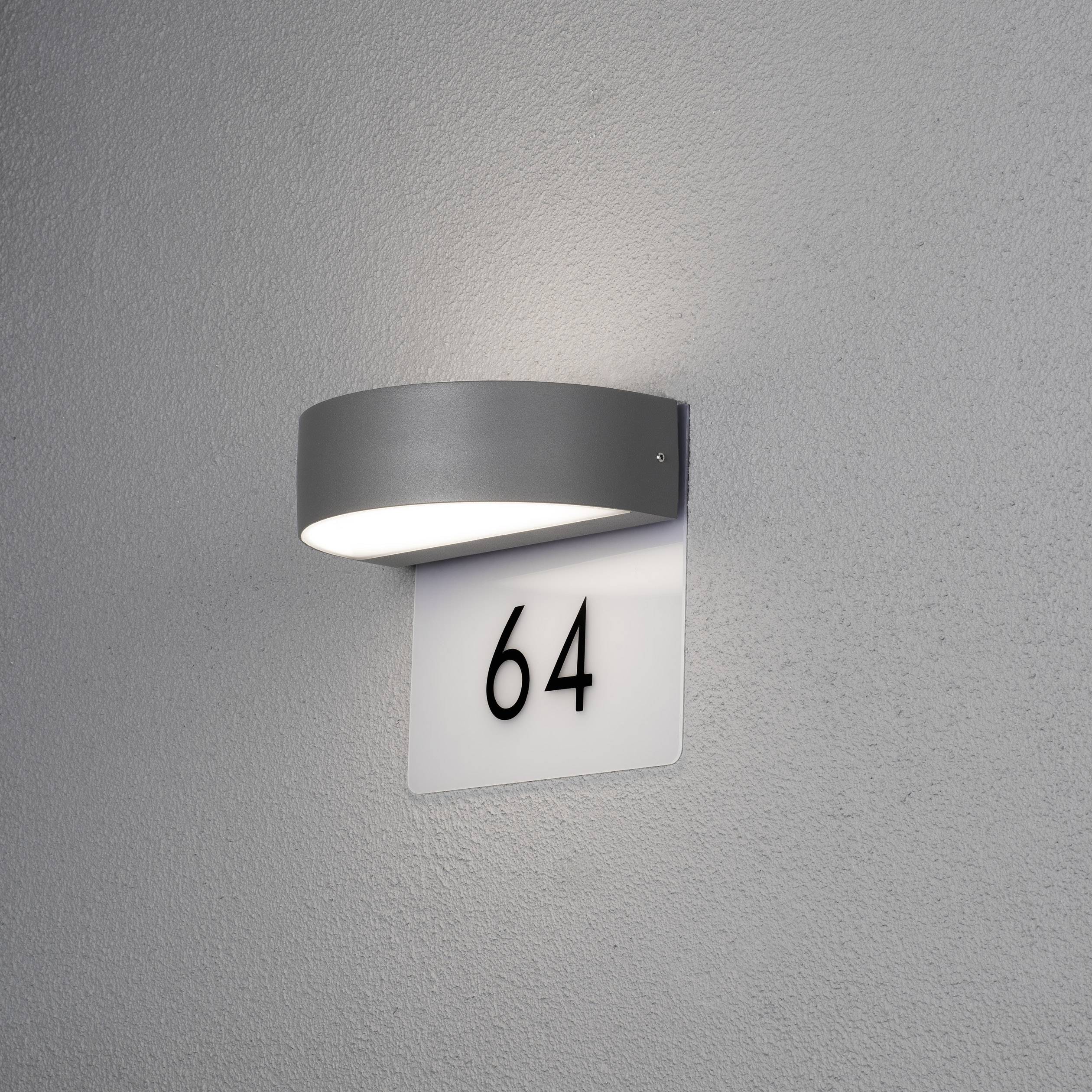 Außenwandleuchte beleuchtet Hausnummer '64' auf weißem Schild an grauer Wand.