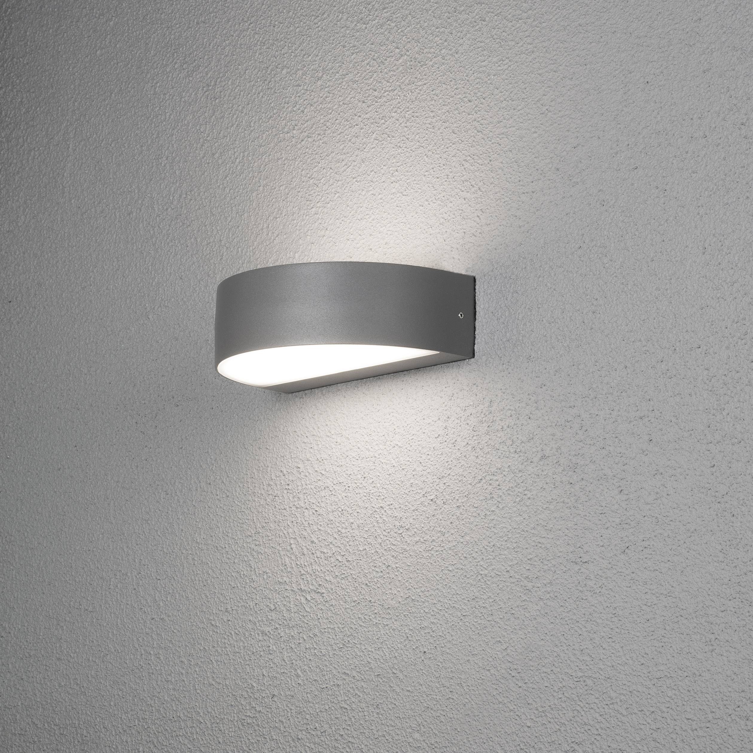 Eine elegante Wandlampe mit modernem Design strahlt diffuses Licht aus und erzeugt einen weichen Lichteffekt auf der grauen Wand.
