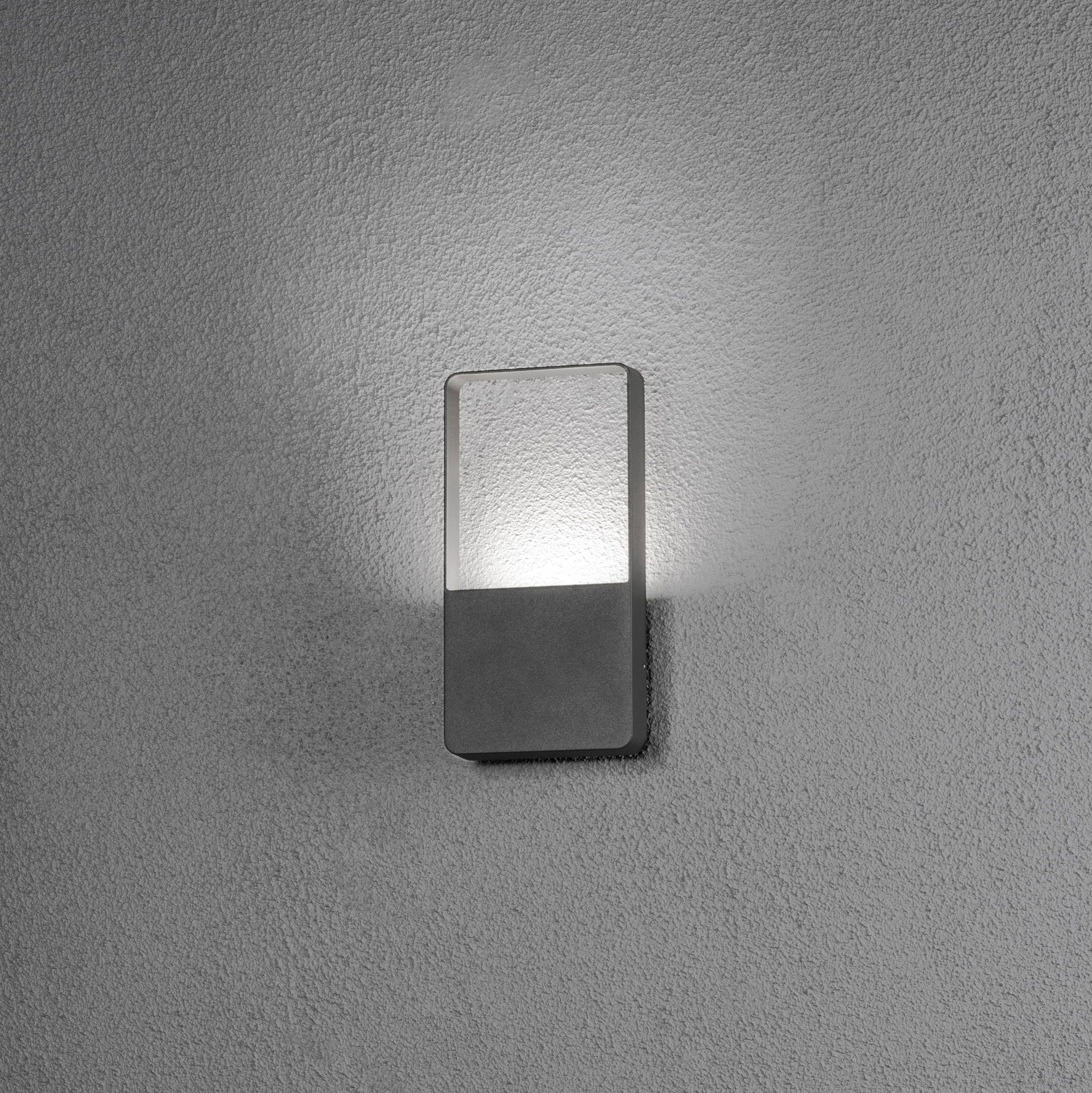 Wandleuchte mit rechteckigem Rahmen, die warmes Licht an einer grauen Wand abstrahlt. Moderne und minimalistische Gestaltung.
