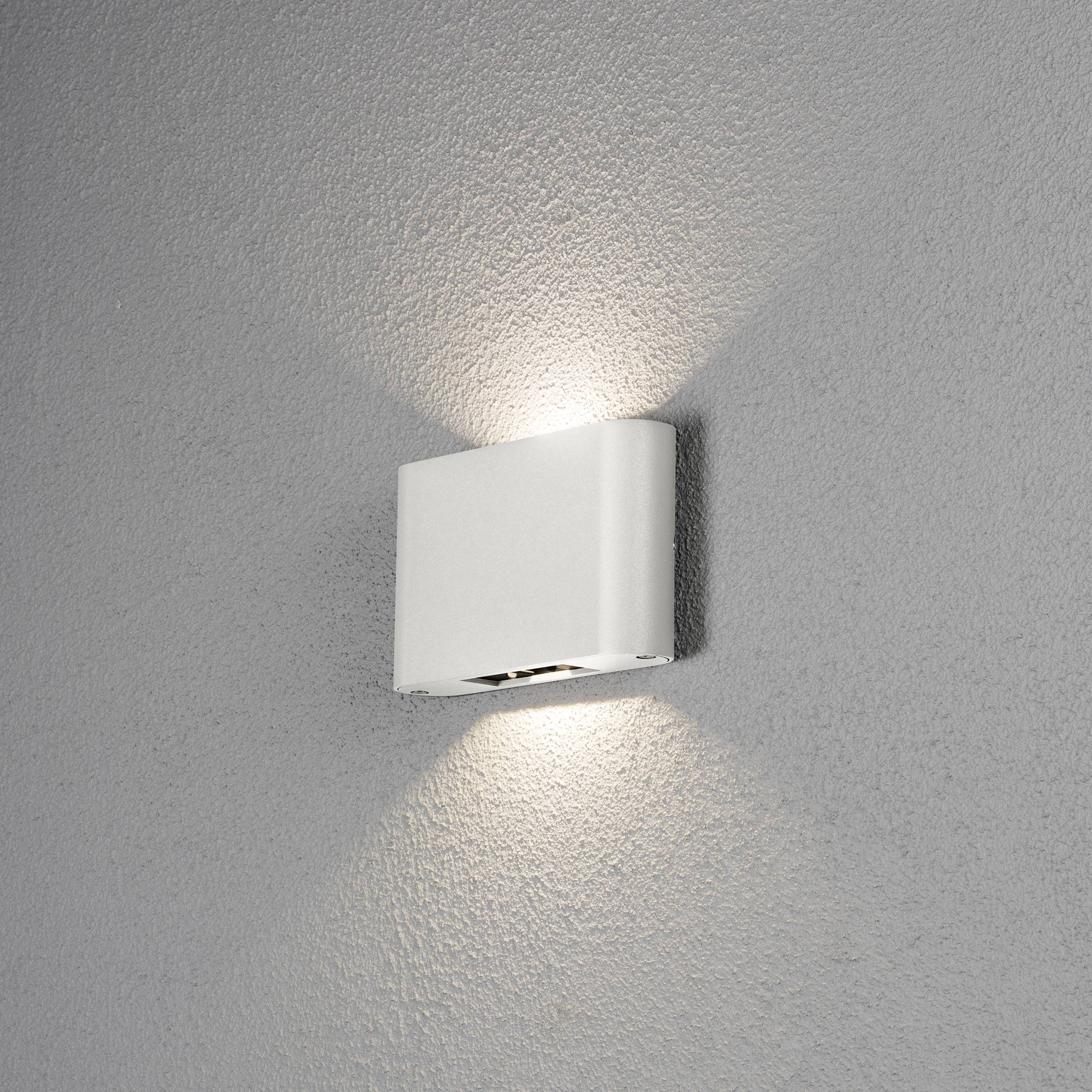 Weiße Wandleuchte an grauer Wand, strahlt Licht nach oben und unten aus, erzeugt ein weiches Ambiente.