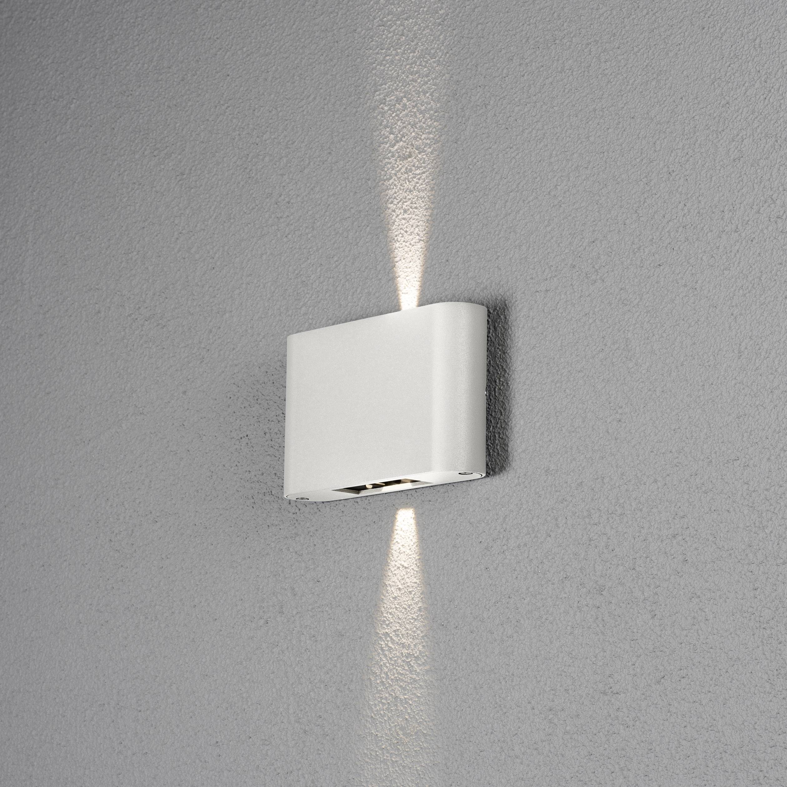 Weiße Wandlampe mit modernem Design, strahlt Licht nach oben und unten an eine graue Wand ab.