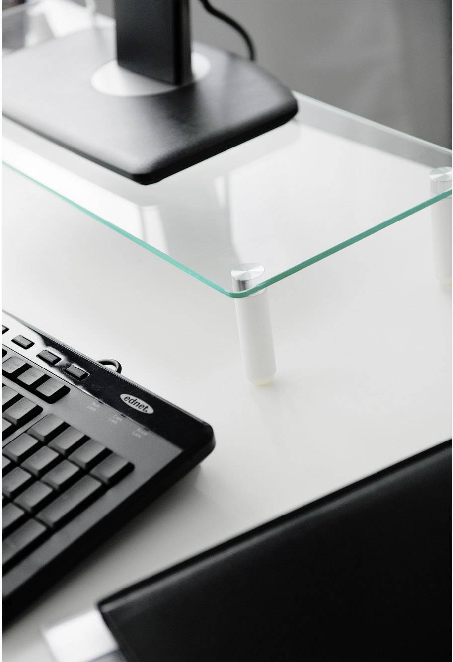 Tastatur auf einem weißen Schreibtisch mit Glasablage und einem Monitorständer. Es vermittelt eine saubere und organisierte Arbeitsumgebung.