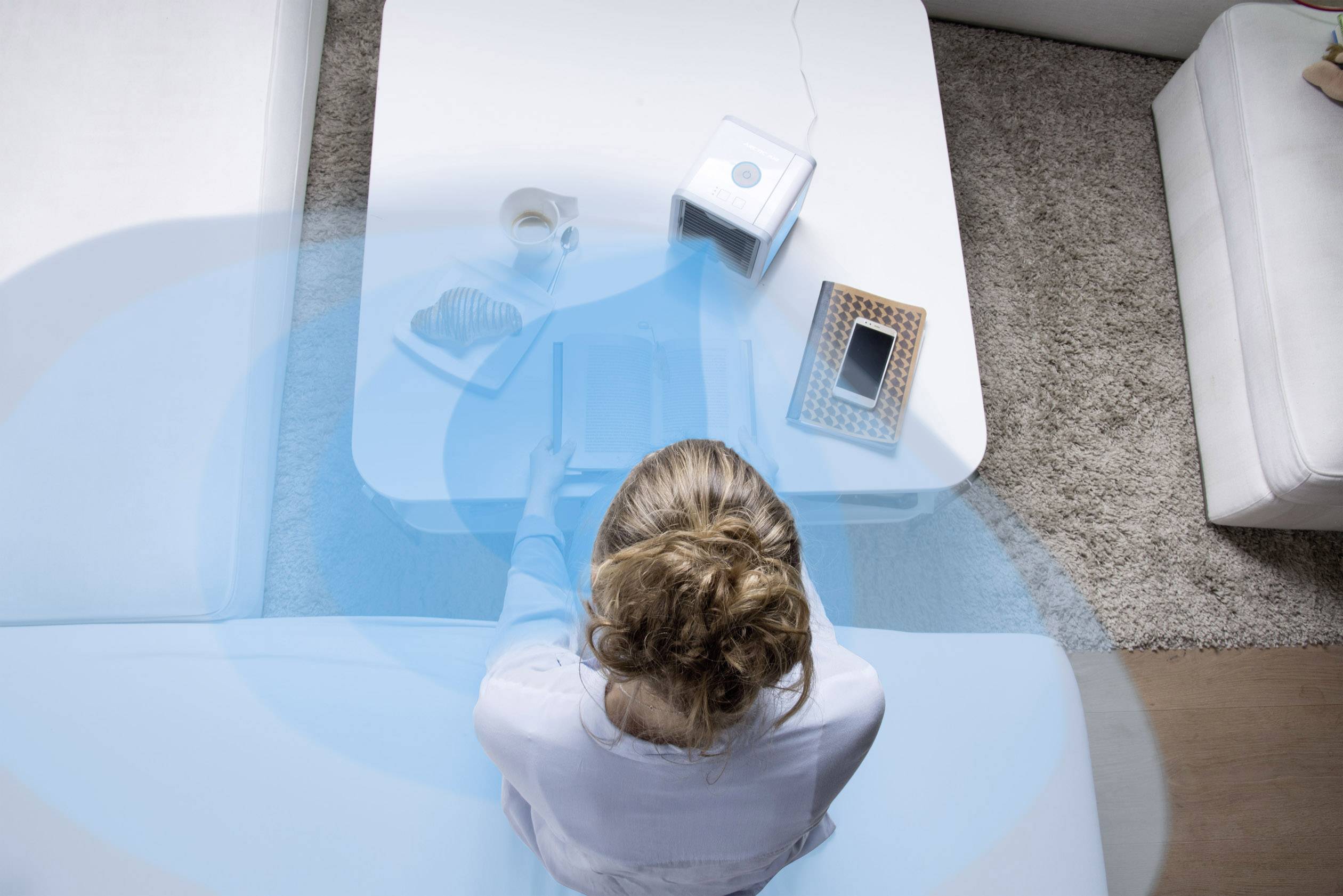 Eine Person sitzt auf einem Sofa, Blick aus der Vogelperspektive. Vor ihr auf dem Tisch liegen diverse Gegenstände, darunter ein Smartphone.
