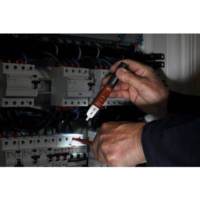 Eine Person prüft mit einem berührungslosen Spannungsprüfer Kabel in einem elektrischen Schaltschrank auf Spannung.