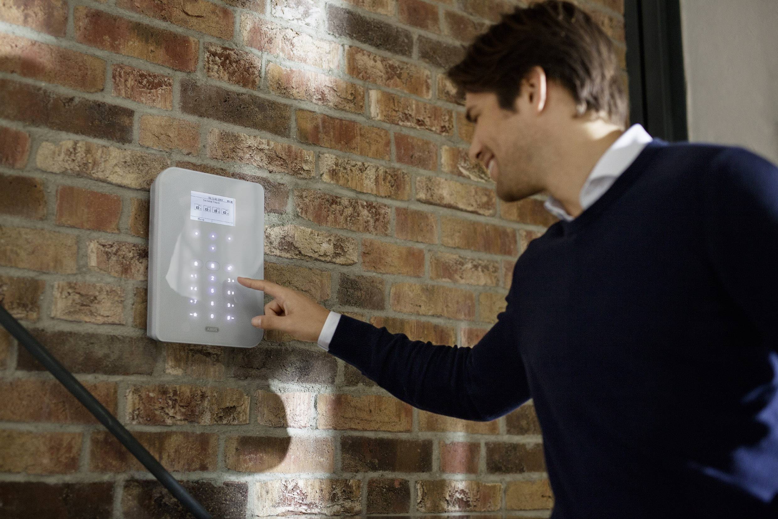 Ein Mann bedient ein digitales Zugangsterminal an einer Backsteinwand, das mit leuchtenden Tasten zur Eingabe eines Codes ausgestattet ist.