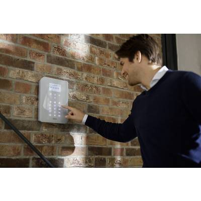 Ein Mann bedient ein digitales Zugangsterminal an einer Backsteinwand, das mit leuchtenden Tasten zur Eingabe eines Codes ausgestattet ist.