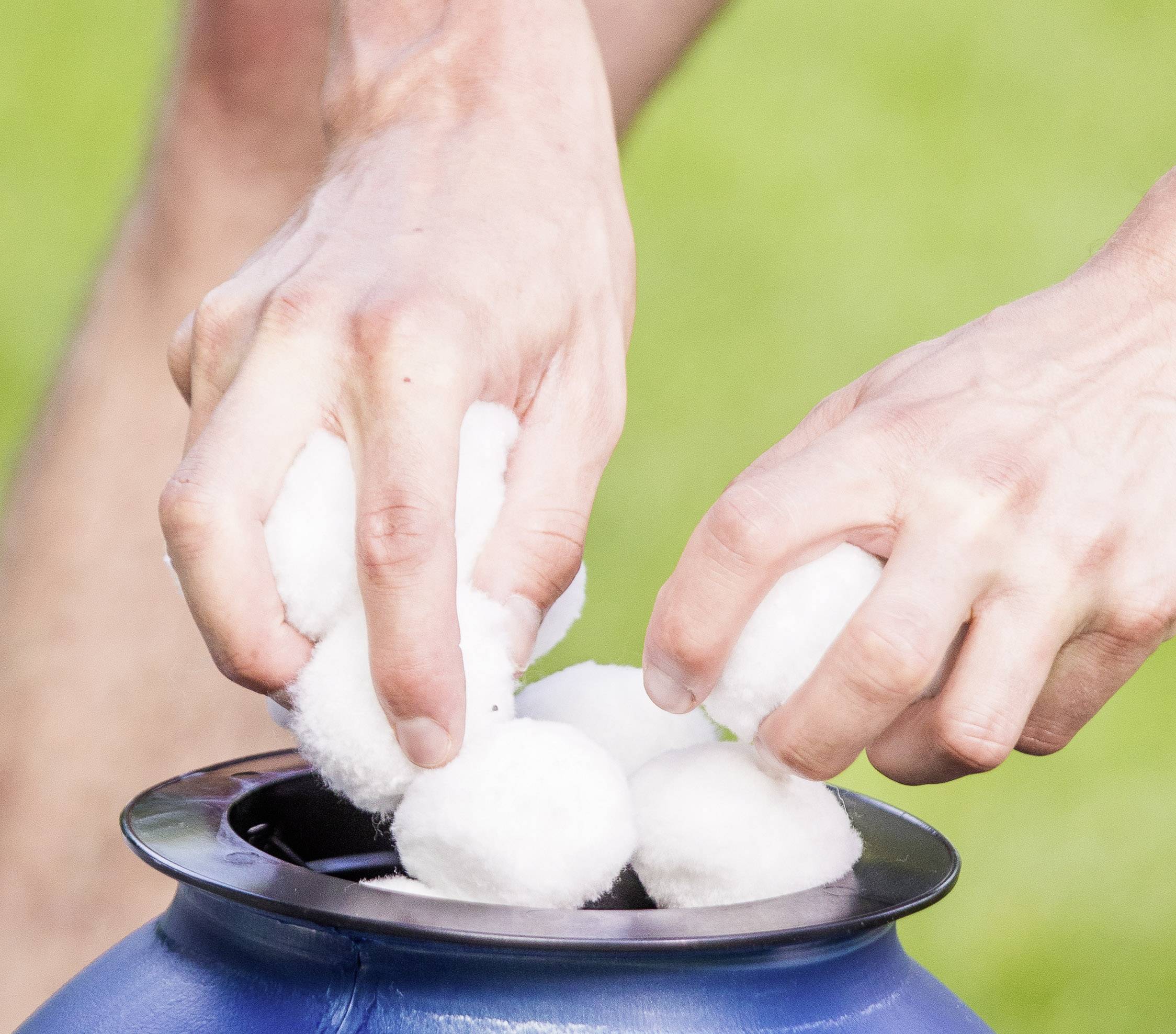 Hände eines Menschen legen weiße Wattebäusche in einen blauen Behälter im Freien.