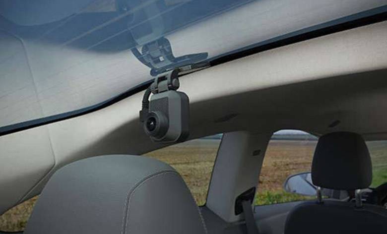 Autokamera an der Windschutzscheibe eines Fahrzeugs montiert, zeigt einen Innenraum mit teilweisem Blick auf die Landschaft draußen.