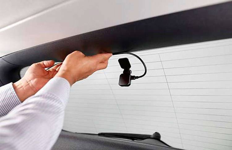 Eine Person installiert eine Dashcam an der Heckscheibe eines Autos. Die Kamera ist kompakt und wird an der Innenseite befestigt.