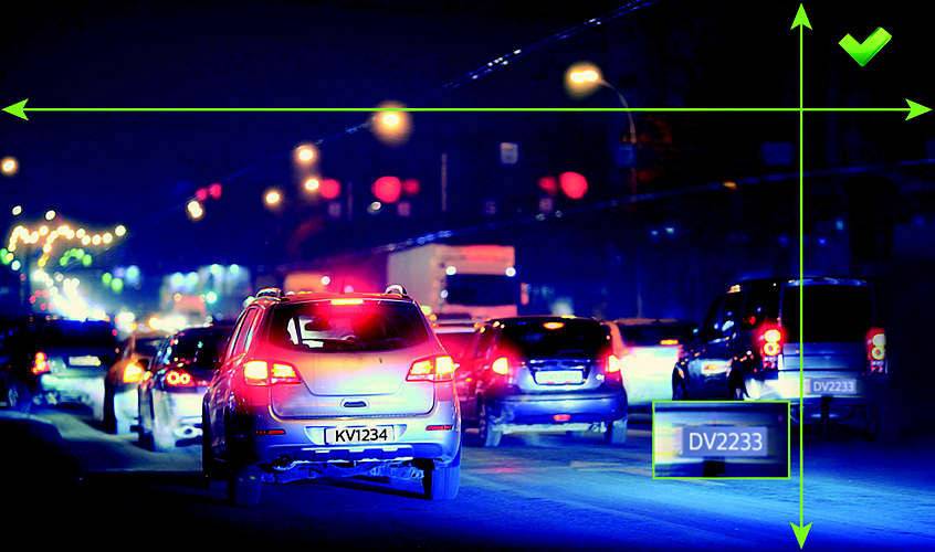 Ein Auto fährt nachts auf einer belebten Straße mit anderen Fahrzeugen. Lichter und Nummernschilder sind im Dunkeln sichtbar.