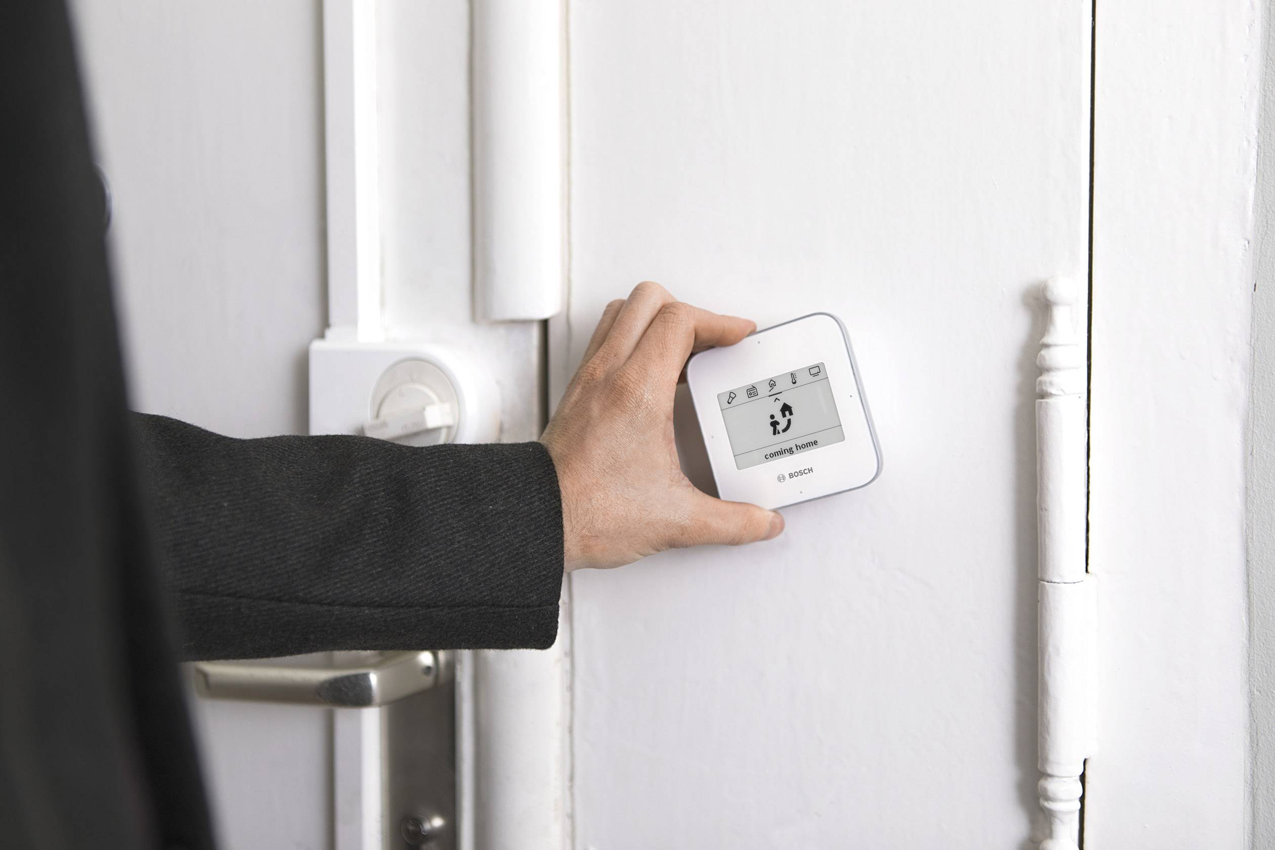 Eine Person in einem Anzug stellt ein digitales Thermostat an einer weißen Wand ein.
