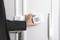 Eine Person in einem Anzug stellt ein digitales Thermostat an einer weißen Wand ein.