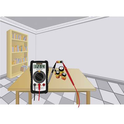 Digitalmultimeter auf einem Tisch zeigt '12.94' an, verbunden mit mehreren Batterien. Hintergrund: Bücherregal in einem Raum.