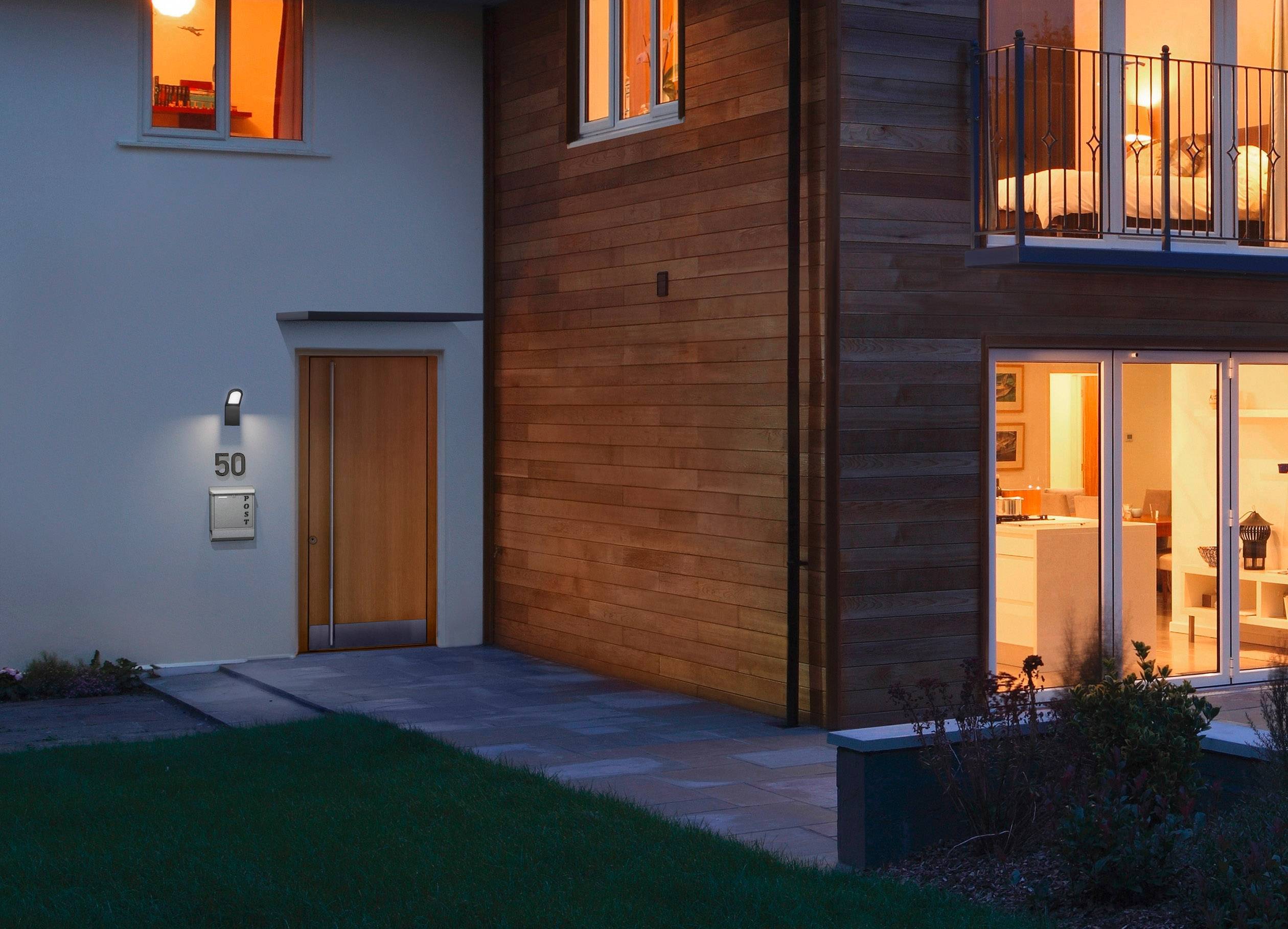 Eingangsbereich eines modernen Hauses bei Abenddämmerung, beleuchtete Fenster zeigen warmes Innenlicht. Hausnummer '50'.