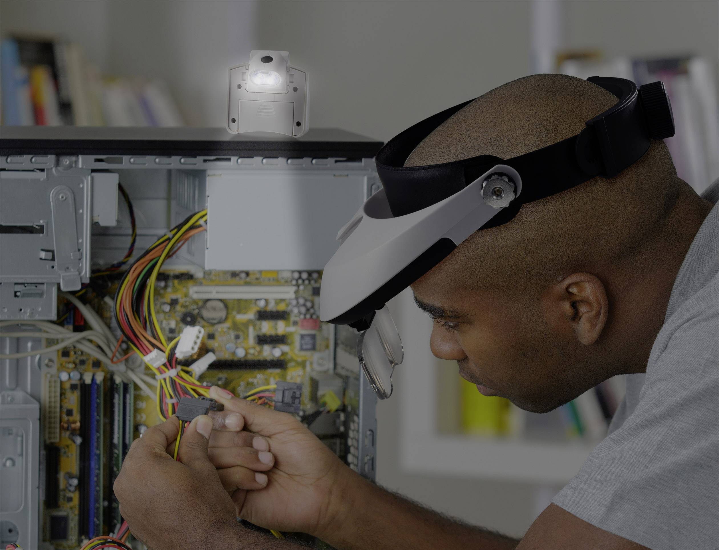 Ein Mann repariert das Innere eines Computers mit einem Werkzeug in der Hand. Er trägt ein Stirnband mit Lupe, konzentriert arbeitend.