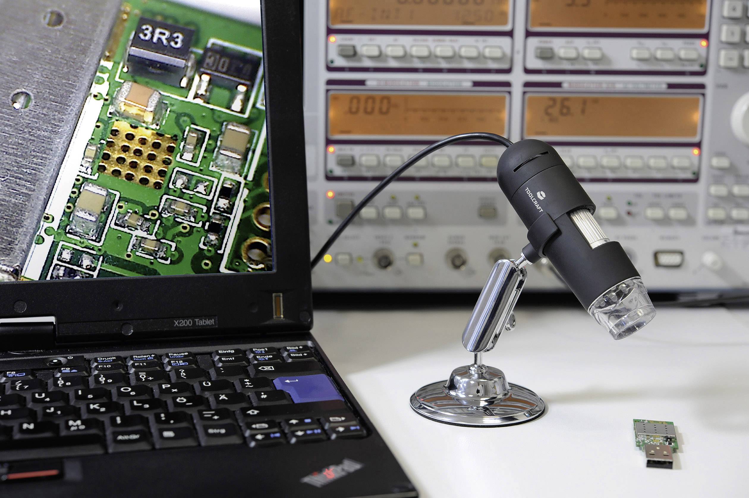 Ein Mikroskop mit Kamera ist auf eine elektronische Platine ausgerichtet, die auf einem Laptop-Bildschirm vergrößert gezeigt wird. Im Hintergrund sind Messgeräte sichtbar.