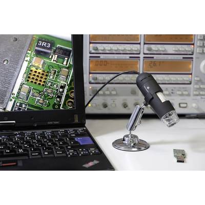 Ein Mikroskop mit Kamera ist auf eine elektronische Platine ausgerichtet, die auf einem Laptop-Bildschirm vergrößert gezeigt wird. Im Hintergrund sind Messgeräte sichtbar.