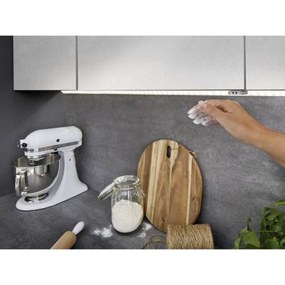 Hand streut Mehl über die Arbeitsfläche in moderner Küche. Ein Mixer, ein Glas Mehl und Holzbretter sind sichtbar.