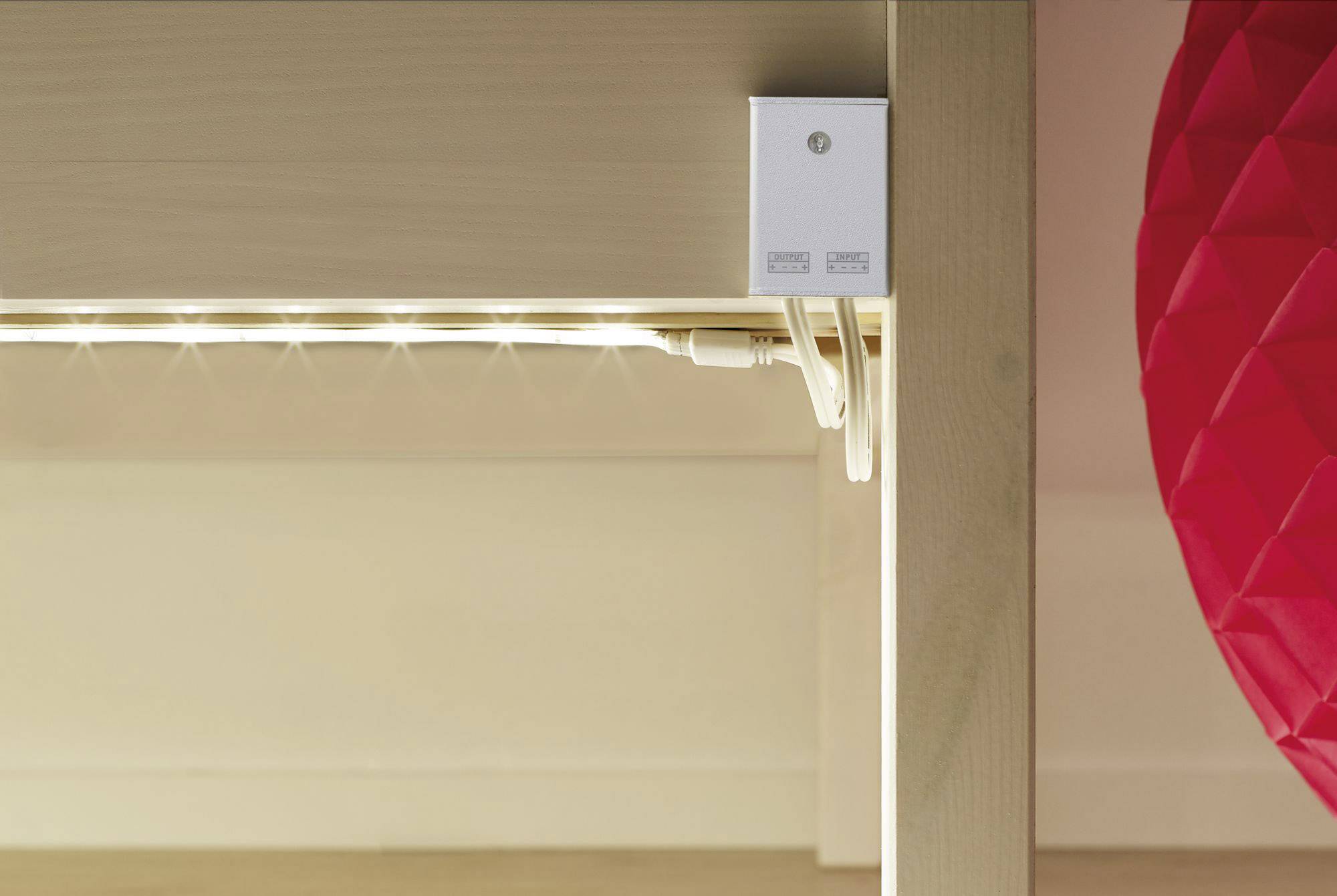 Unter einem Tisch ist eine LED-Lichtleiste montiert. Neben der Lichtleiste befindet sich ein rotes, strukturiertes Objekt.