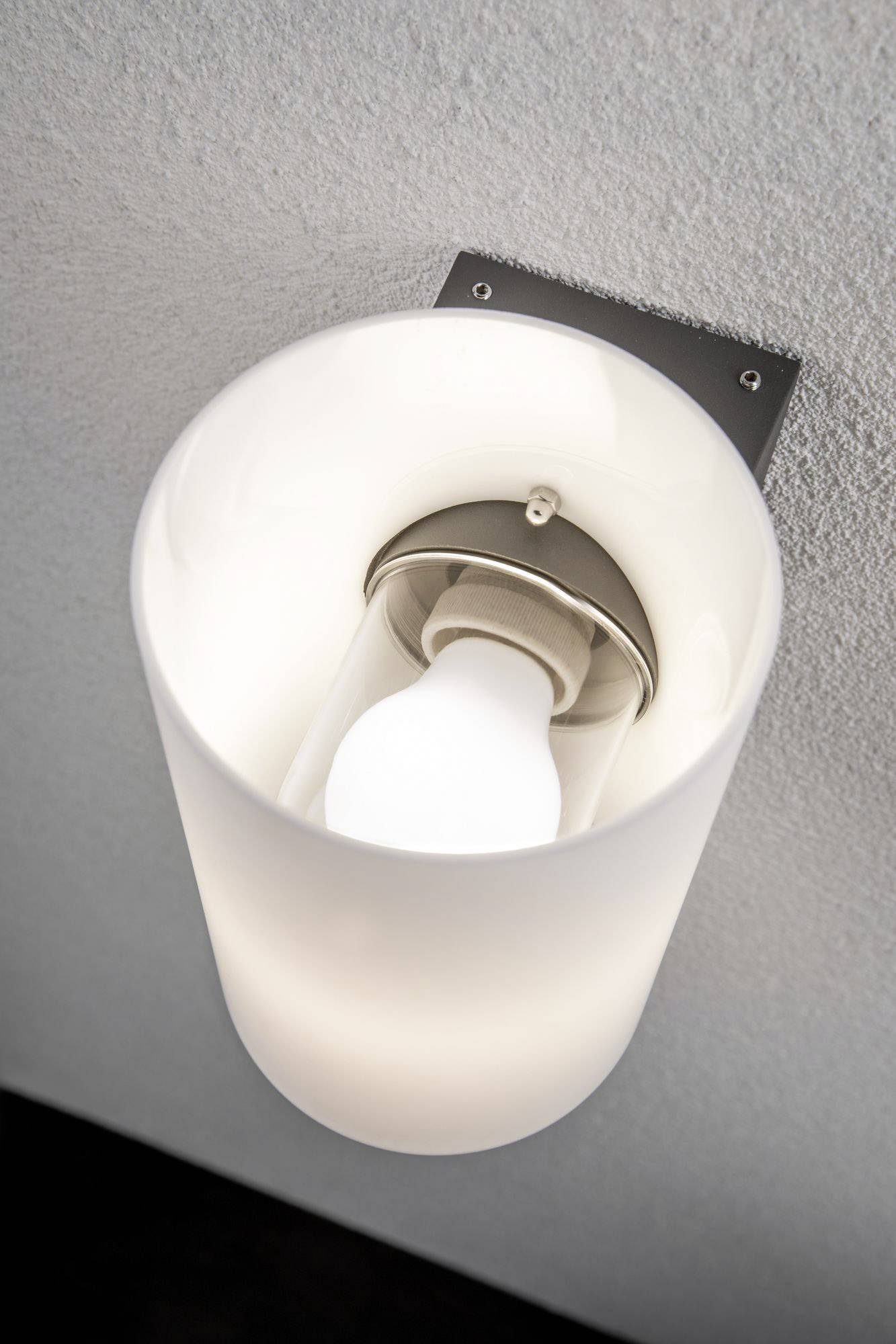 Eine Wandlampe mit einem matten, weißen Schirm, der eine Glühbirne bedeckt, und einem flachen, rechteckigen Metallhalter.