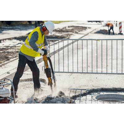 Arbeiter mit Schutzkleidung bohrt mit Presslufthammer auf Baustelle. Absperrung im Hintergrund.