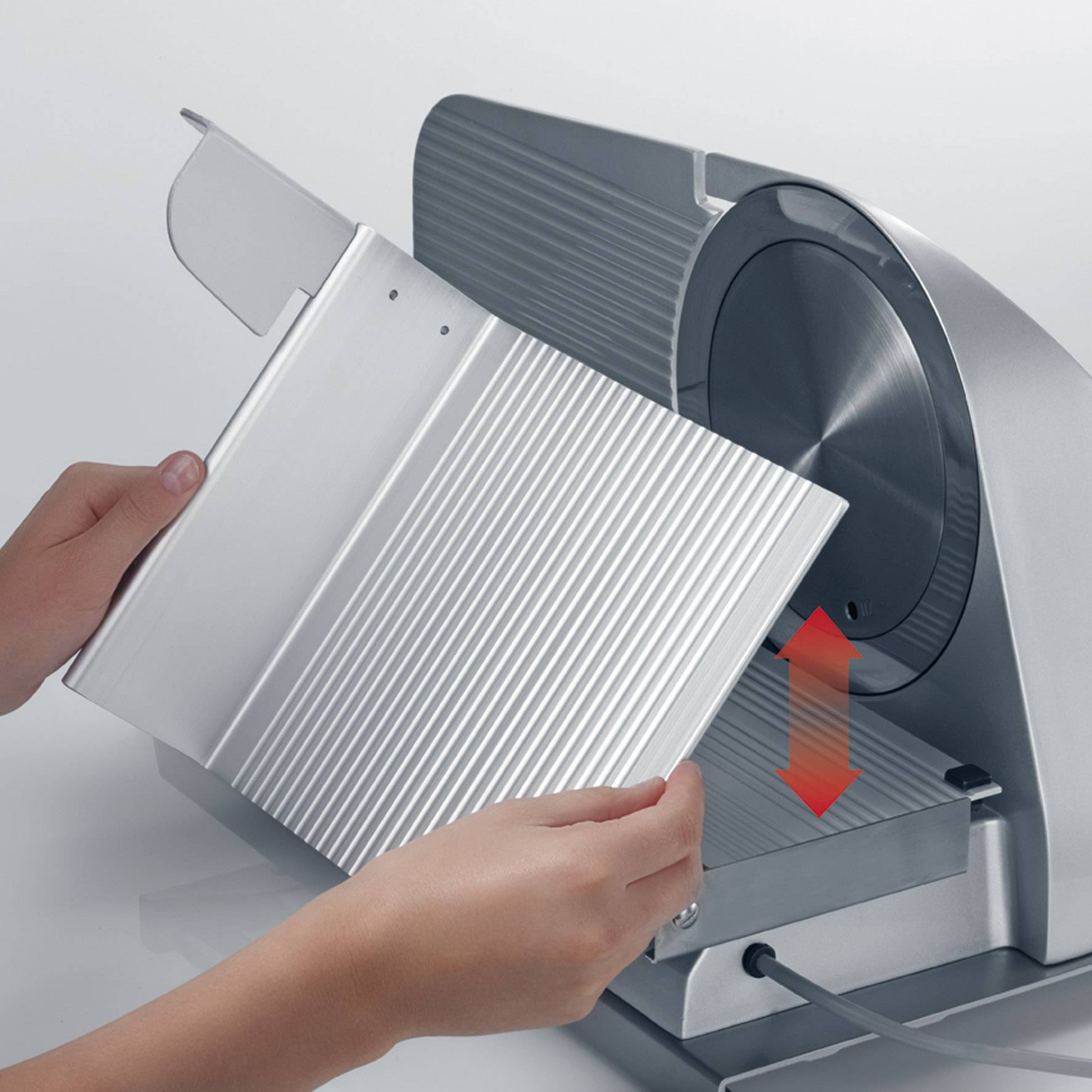 Person bedient eine silberne Aufschnittmaschine, die einen roten Pfeil für die Schnittführung zeigt. Sie hält eine Platte zum Schneiden.