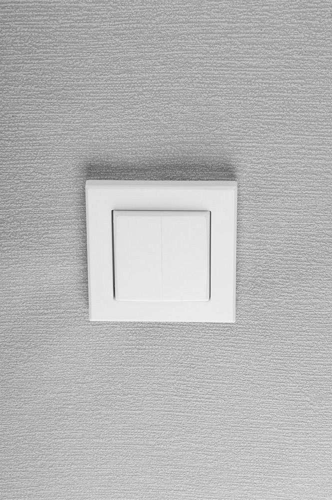Ein weißer Lichtschalter an einer grauen Wand.