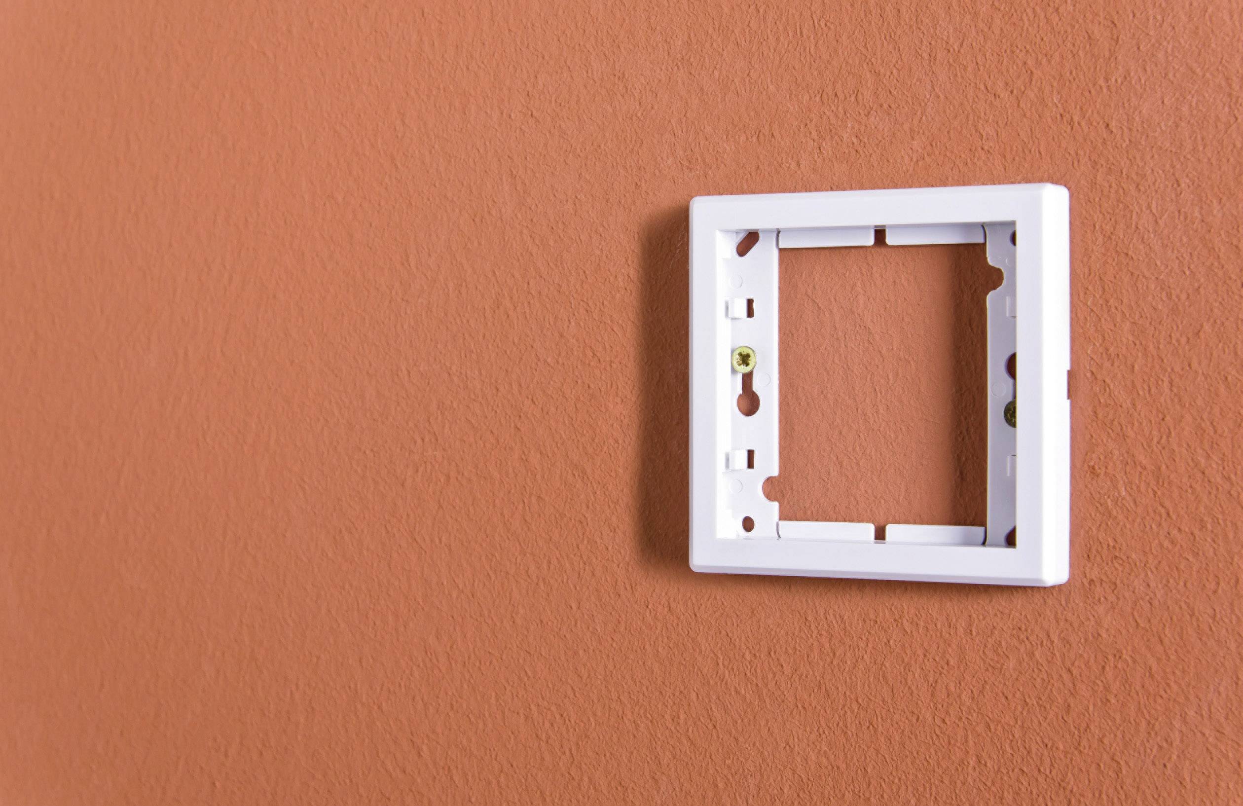 Leerer, weißer Lichtschalterrahmen an einer orangefarbenen Wand, ohne Schalterelemente.