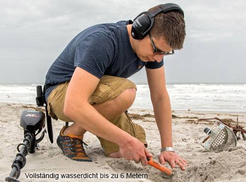 Ein Mann mit Kopfhörern benutzt einen Metalldetektor am Strand. Der Text im Bild lautet: 'Vollständig wasserdicht bis zu 6 Metern'.