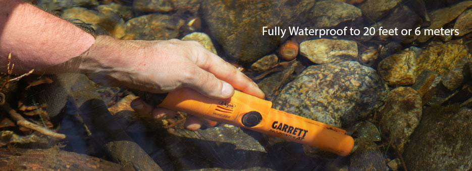 Eine Hand hält einen orangefarbenen Metalldetektor unter Wasser in einem Bach. Text sagt: 'Vollständig wasserdicht bis 6 Meter.'