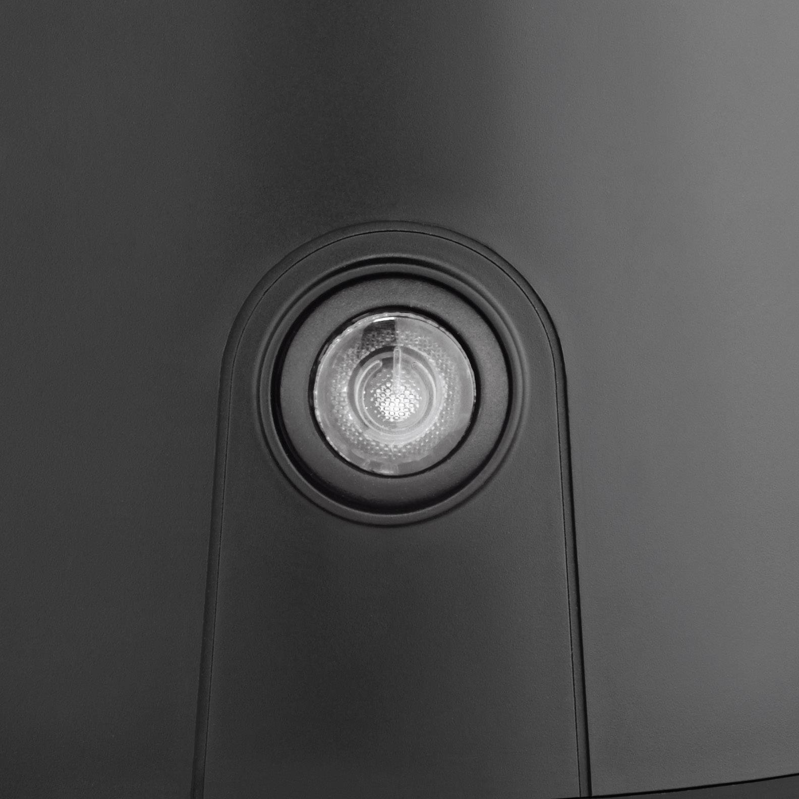 Nahaufnahme eines runden Objektivs in einem schwarzen Gehäuse, möglicherweise eine Kamera oder ein Sensor. Hintergrund glatt und dunkel.