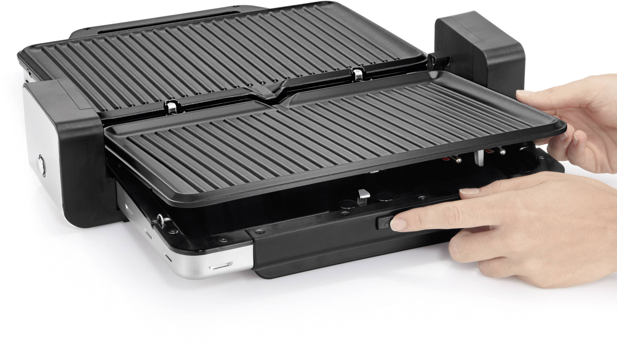 Eine Person bedient einen elektrischen Kontaktgrill, indem sie den Einschaltknopf drückt. Grillplatten sind geöffnet und leer.