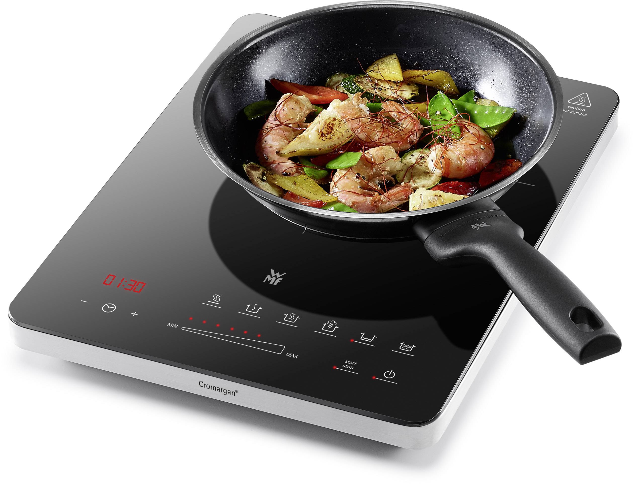 Eine elektrische Kochplatte mit einer Pfanne darauf. In der Pfanne braten Garnelen mit Gemüse. Die Kochplatte zeigt eine Temperaturanzeige.