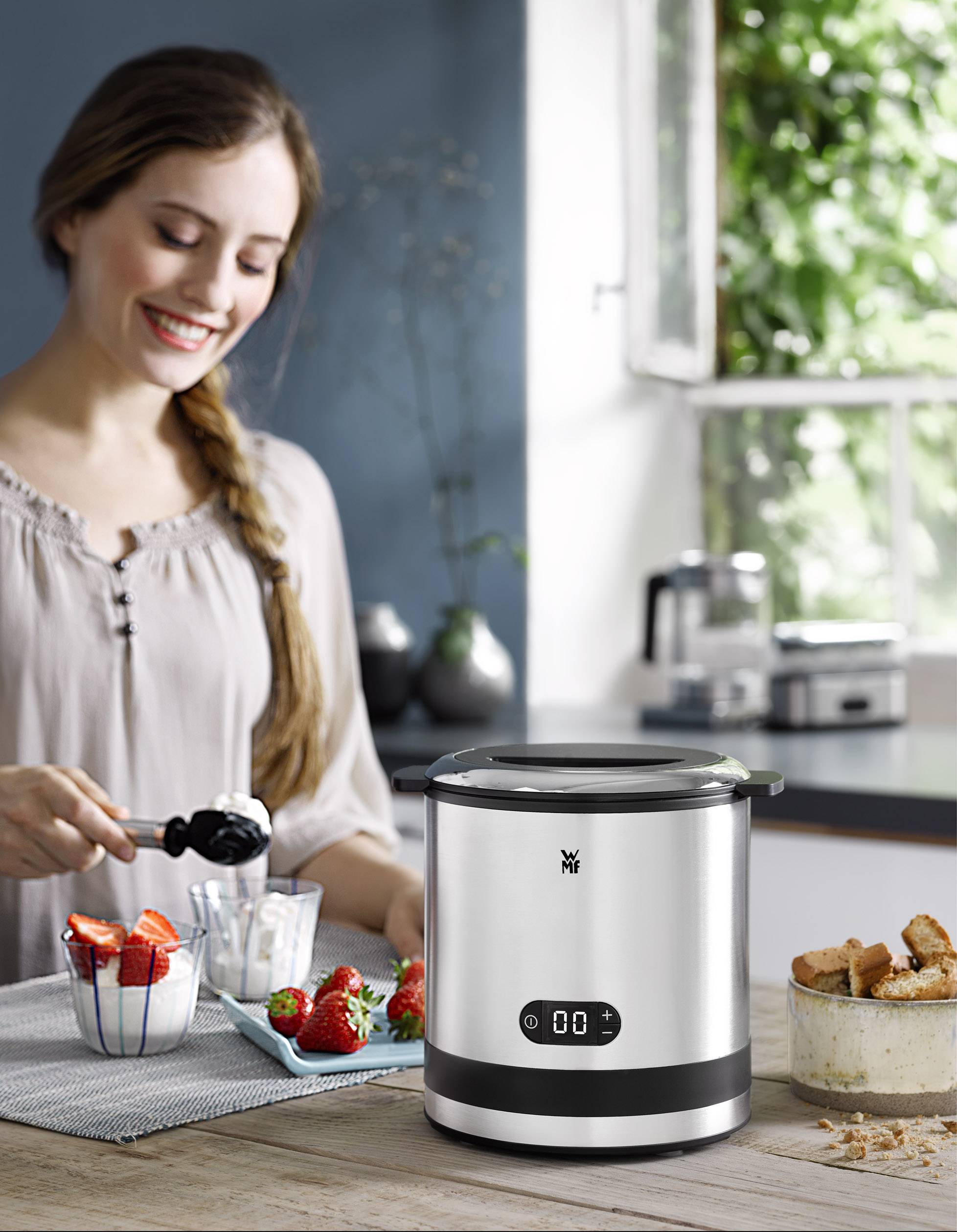 Eine Frau bereitet Joghurt mit einer Joghurtmaschine in einer modernen Küche zu. Sie misst Zutaten ab.