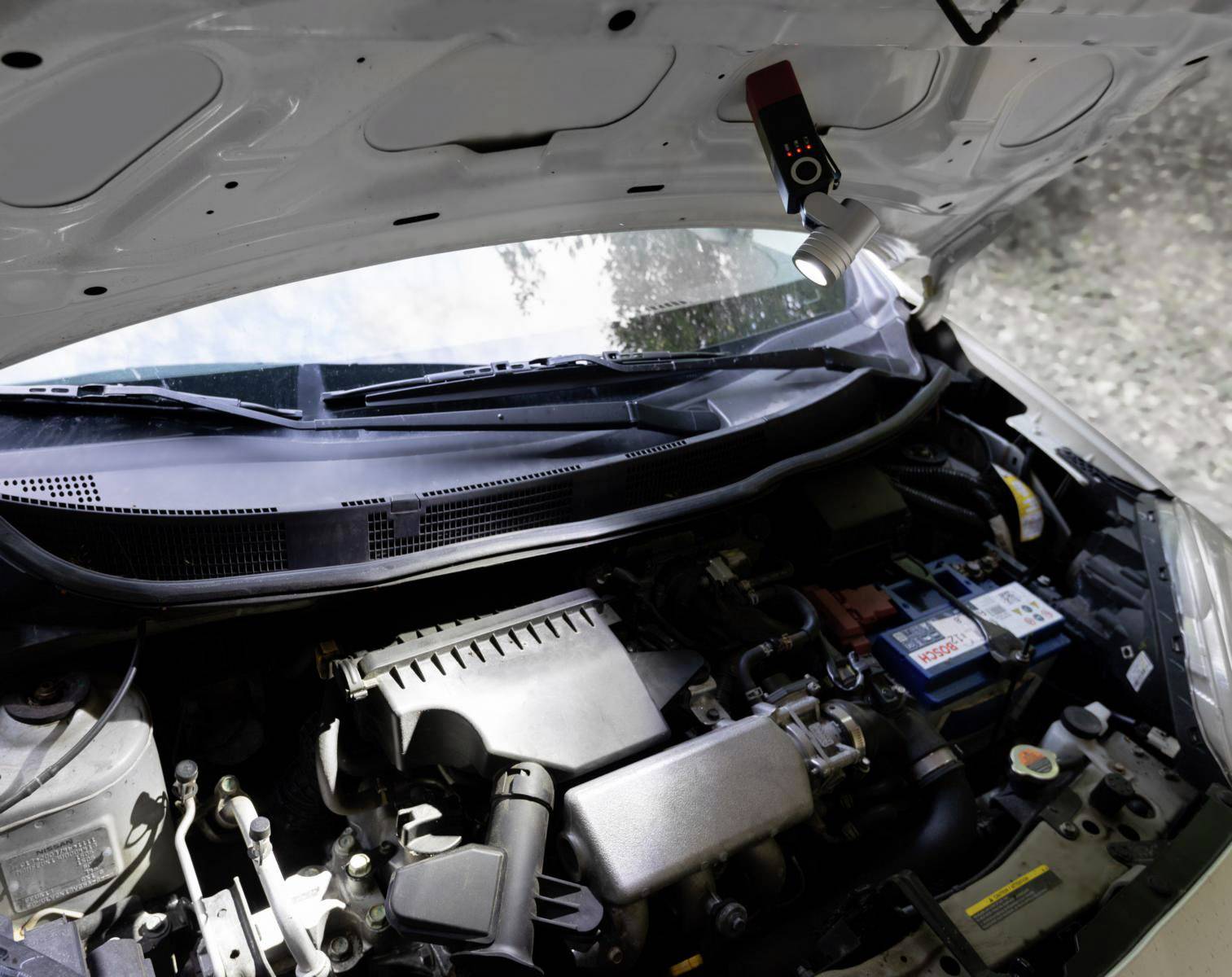 Das geöffnete Auto zeigt den Motorraum eines weißen Fahrzeugs. Ein Diagnosegerät ist an der Innenseite der Motorhaube befestigt.