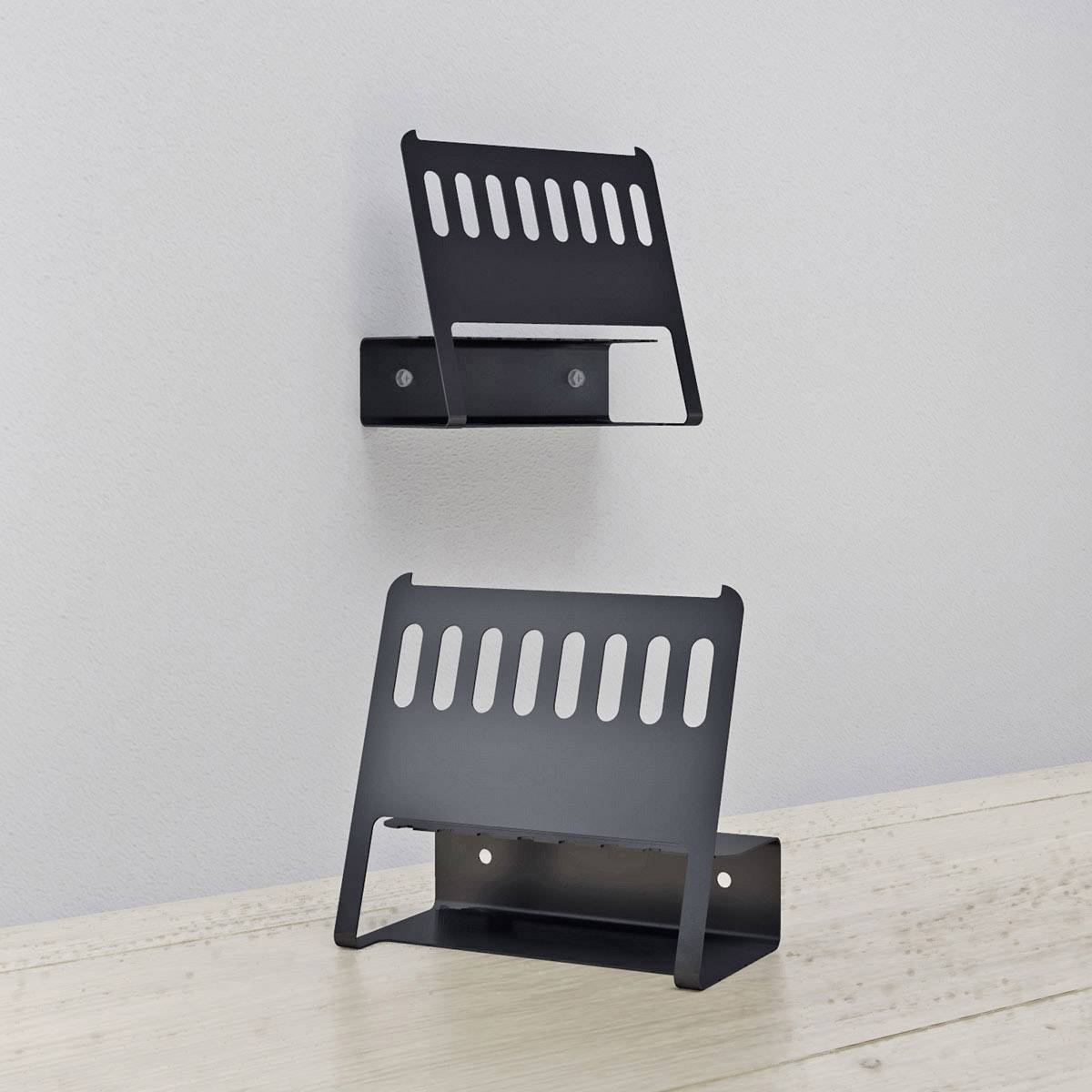 Zwei schwarze, wandmontierte Kabelhalter aus Metall auf einer weißen Wand und einem Holztisch; halten Kabel ordentlich an Ort.