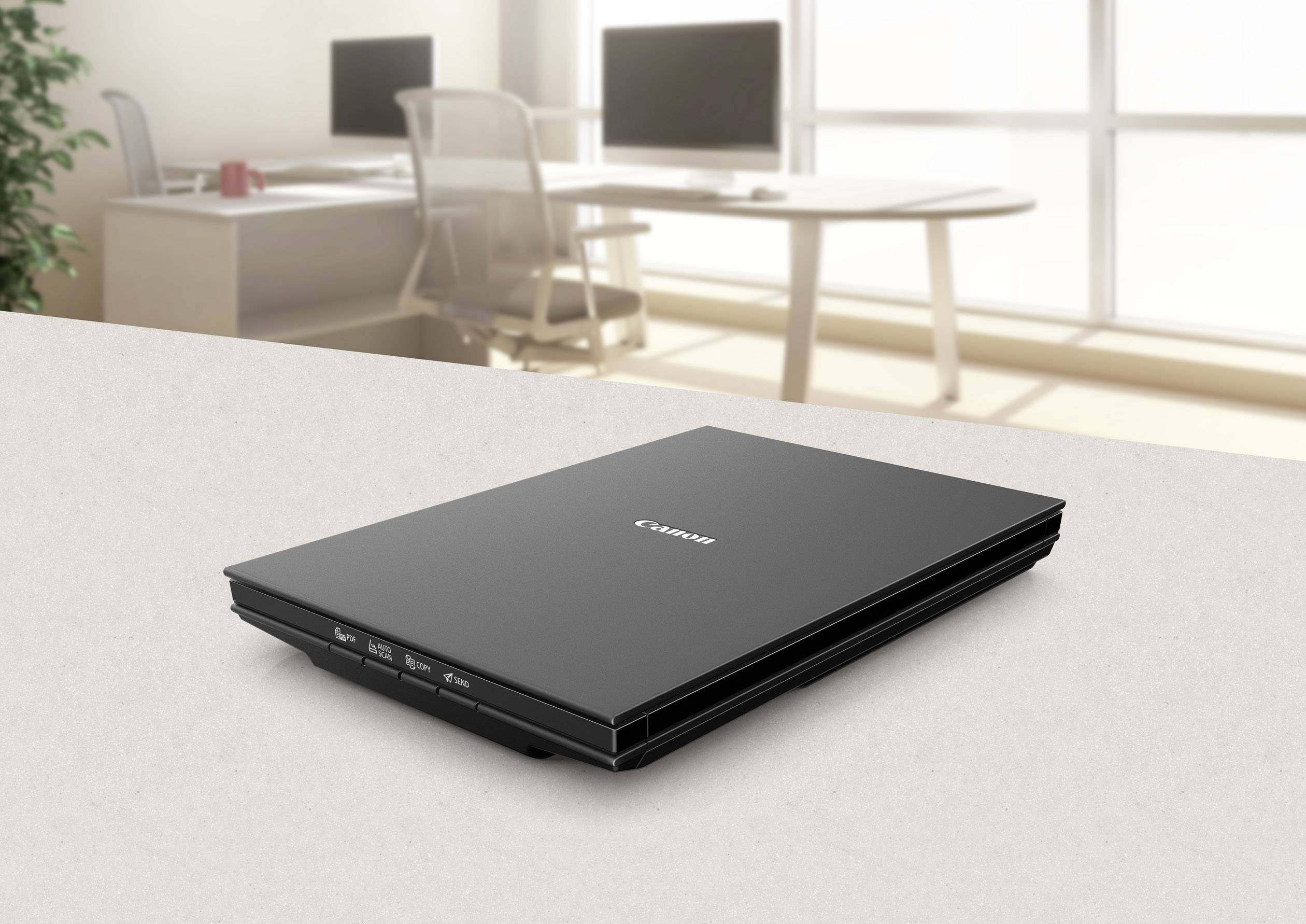 Ein flacher Scanner auf einem Tisch in einem hellen Büro. Im Hintergrund sind Schreibtische und Stühle sichtbar.