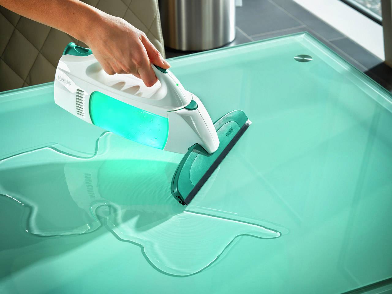 'Eine Person reinigt eine Glasfläche mit einem elektrischen Fensterreiniger. Die Flüssigkeit wird gleichmäßig entfernt.'