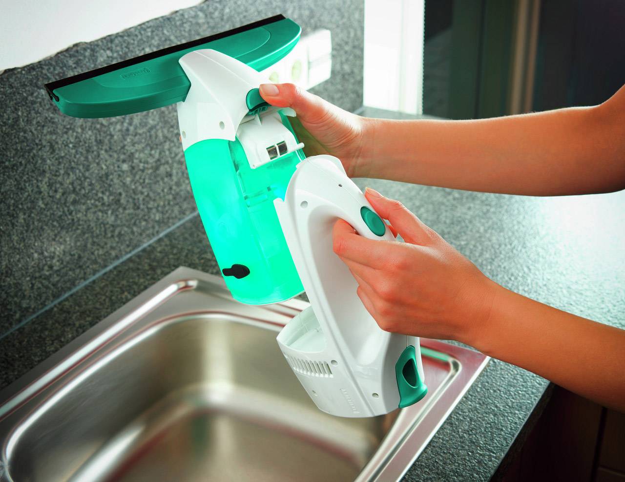 Person hält ein Fensterreinigungsgerät über einem Spülbecken, während sie den Wassertank entleert. Gerät hat einen grünen und weißen Farbakzent.