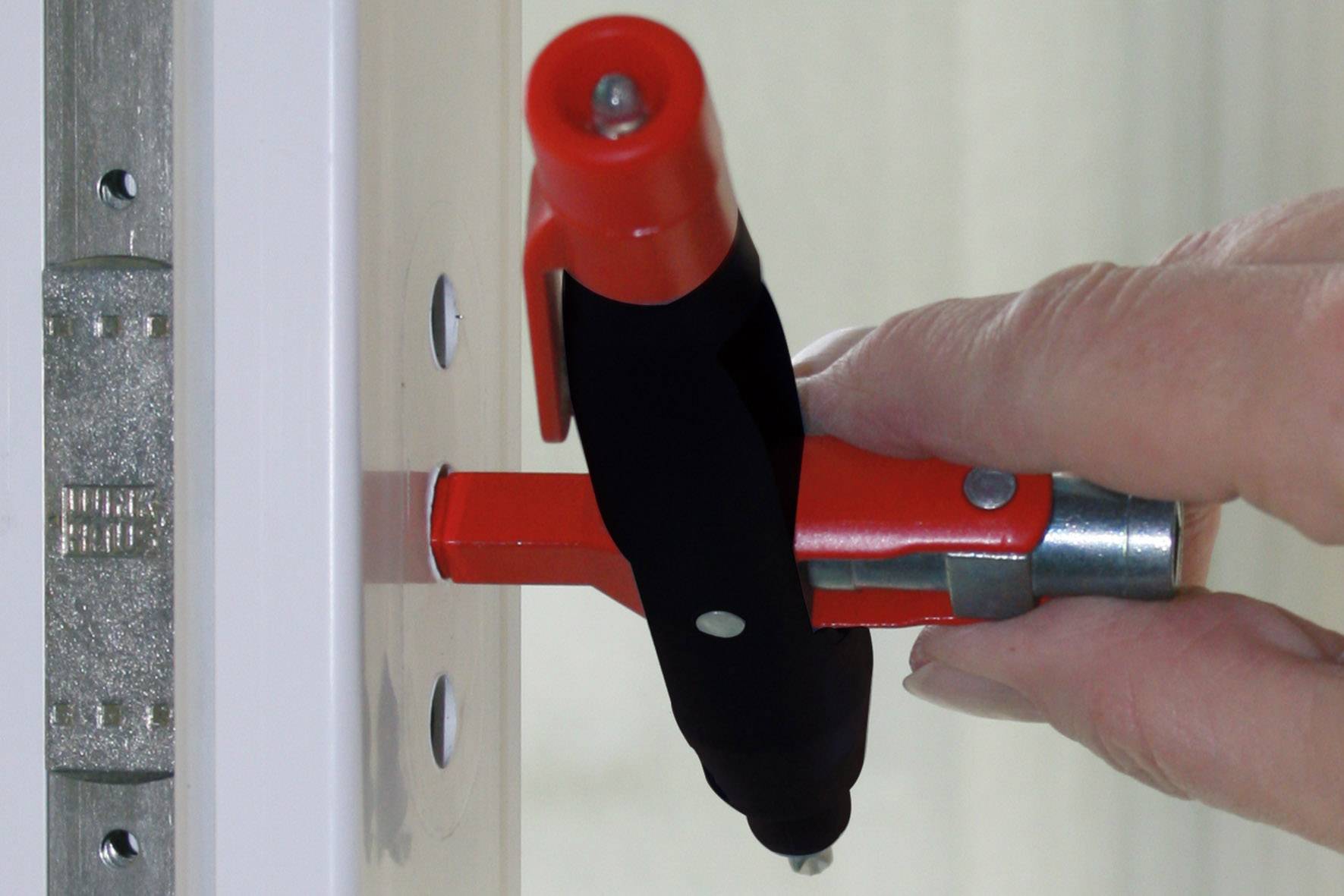Eine Person dreht einen roten Sicherheitsriegel, der an einer weißen Tür angebracht ist. Der Riegel ist zur Diebstahlsicherung.