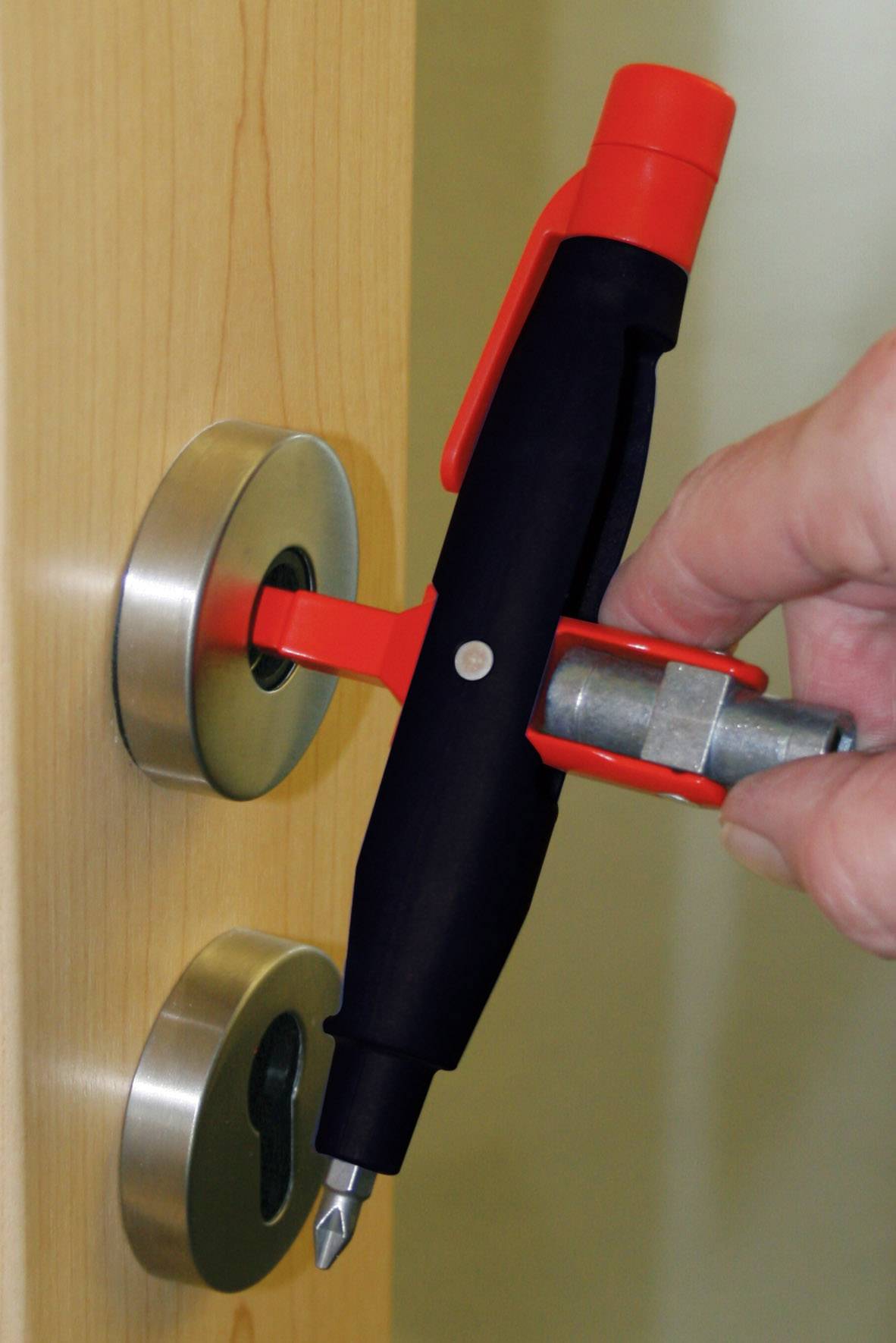 Hand verwendet ein Werkzeug, um ein Schloss in einer Tür zu manipulieren. Das Werkzeug ist rot und schwarz und wird ins Schloss gehalten.