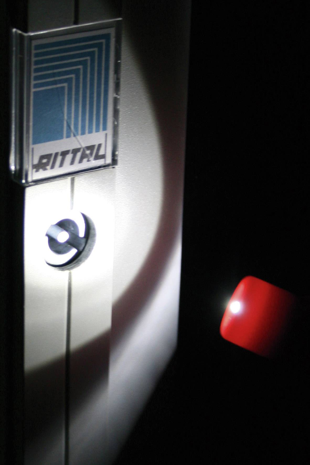 Eine Tür eines Rittal-Schranks wird im Dunkeln mit einer Taschenlampe beleuchtet, die auf das Schloss und das Rittal-Logo gerichtet ist.