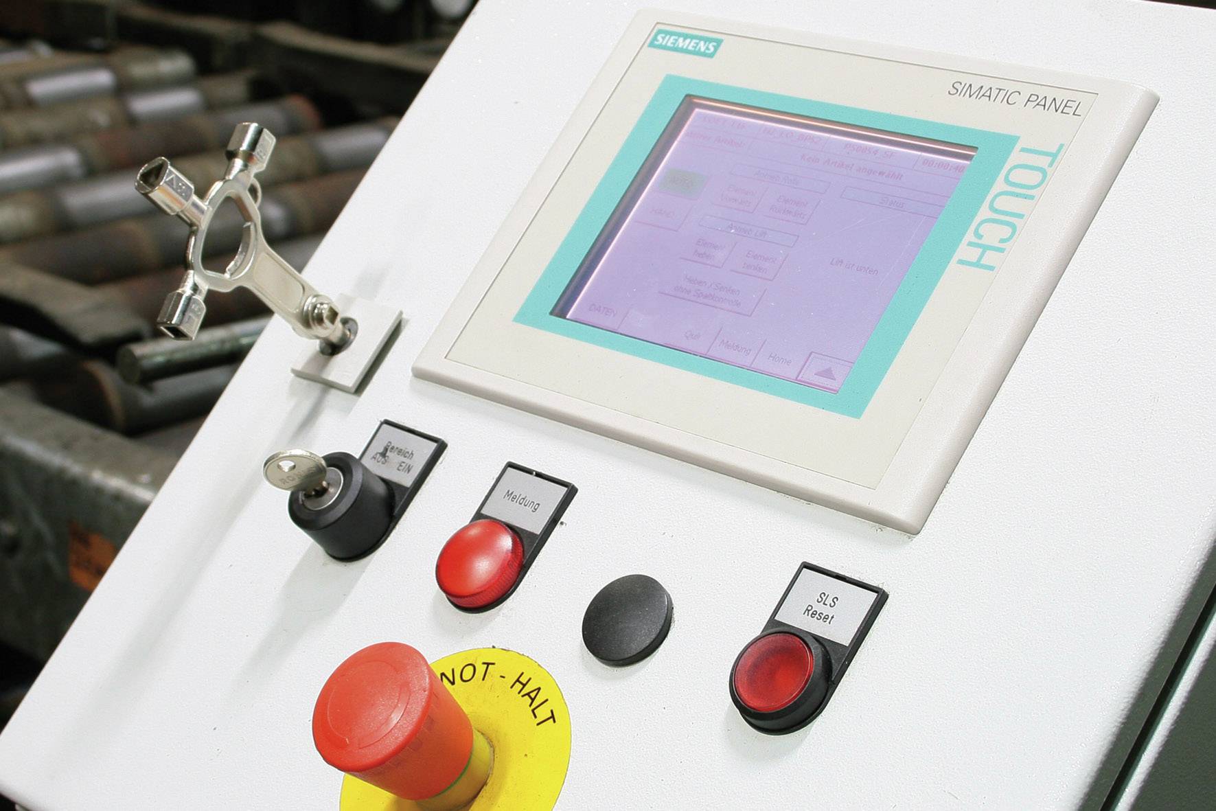 Bedienfeld mit Touchscreen und mehreren Tasten, darunter ein großer roter Knopf mit 'Not-Halt'. Industrielle Steuerungseinheit.