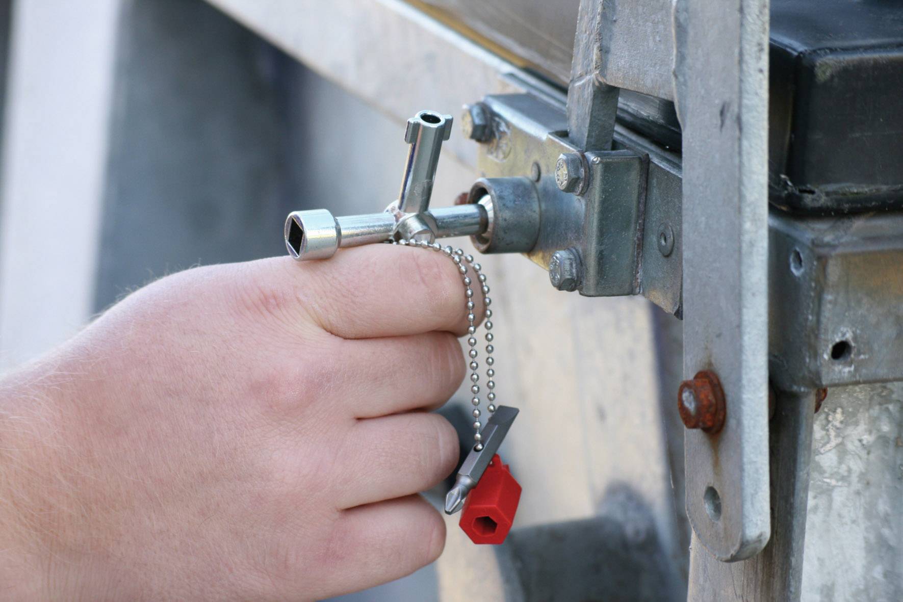 Eine Hand benutzt einen speziellen Vierkantschlüssel, um ein Schloss an einem Metallkasten zu öffnen.